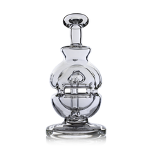 The MJ Arsenal Royale Vape Edition, a clear glass decanter with curved and intersecting glass elements inspired by dab rigs, stands upright on a reflective surface against a plain white background.
