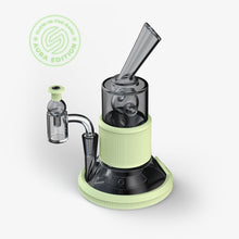 The SOFTGLASS AURA TANDEM RIG in black and light-green glass features glow-in-the-dark accents, silicone sleeves, and is labeled as the Glow-in-the-Dark Aura Edition, shown against a white background.