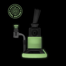 The SOFTGLASS AURA TANDEM RIG is a black glass dab rig with glow-in-the-dark green accents on the base and midsection, featuring a circular Aura Edition logo. Includes protective silicone sleeves.