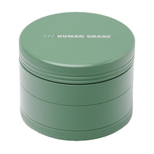 A green, cylindrical aluminum Human Grade Grinder 4C (2.5") with textured edges and "HUMAN GRADE" printed in white on the top lid.