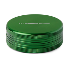 The Human Grade Grinder 1C (2.5" 2-Piece) is a round, metallic green aluminum grinder with textured edges and "HUMAN GRADE" engraved on the flat top.