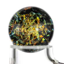 A close-up of a glass marble with colorful shards inside on a clear stand, displayed next to the MJ Arsenal Full Weld Quartz Terp Slurper, set against a white background.