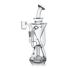 The MJ Arsenal Time Turner Mini Dab Rig, made of clear borosilicate glass, features an intricate design with a bent neck, round base, and side chamber attachment, standing upright on a white background.