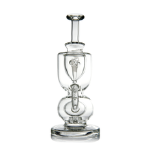 The MJ Arsenal Titan Mini Dab Rig is a clear borosilicate glass rig with an artistic multi-chamber design, smooth rounded shapes, and stands upright on a solid circular base.