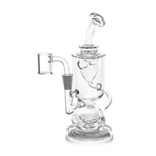 The MJ Arsenal Titan Mini Dab Rig is a clear borosilicate glass piece featuring a cylindrical chamber, curved mouthpiece, round base, and an attached quartz banger for vaporizing concentrates.