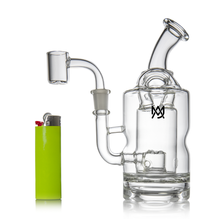The MJ Arsenal Turbine Mini Dab Rig is a clear borosilicate glass water pipe with a cylindrical chamber, angled mouthpiece, side arm, and attached bowl. A bright green lighter stands upright beside it for size comparison.