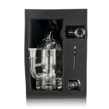The MJ Arsenal Turbine Mini Dab Rig is a clear borosilicate glass set with a main chamber, bowl piece, dab tool, and extra accessory, all securely packed in black foam.
