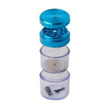 The Human Grade Storage Grinder 1A (2.5") is a blue and clear 4-piece aluminum grinder featuring a metal grinding section, pollen screen, and a storage compartment with a small brush and triangular tool.