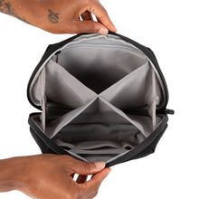 Two hands hold open a PAX Smell Proof Bag, showing its black, water-resistant exterior and a grey interior with four compartments for organized cannabis storage.