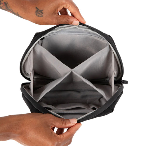 Two hands hold open a PAX Smell Proof Bag, showing its black, water-resistant exterior and a grey interior with four compartments for organized cannabis storage.