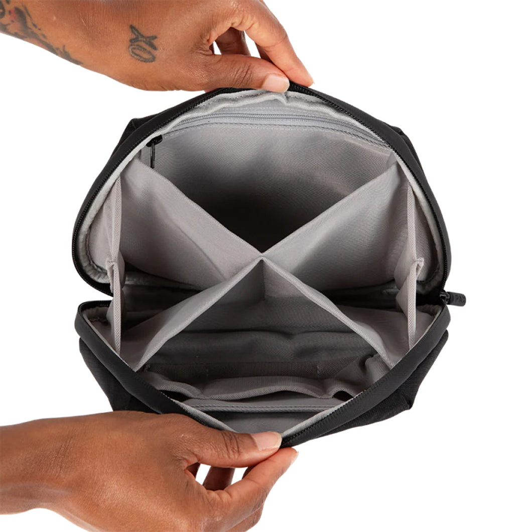 Two hands hold open a PAX Smell Proof Bag, showing its black, water-resistant exterior and a grey interior with four compartments for organized cannabis storage.