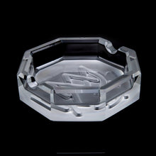The MJ Arsenal Pegasus Ashtray is a clear, octagonal ashtray with grooved edges and a raised design on the base, displayed against a solid black background—perfect for adding luxury to any refined setting.