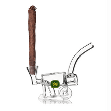 The MJ Arsenal Woodchipper Blunt Bubbler, shaped like a wheelbarrow and made of clear glass, holds large rolled cigars. It features a green emblem with a yellow crown and provides spill-resistant water filtration.