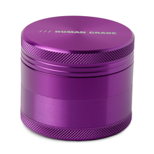 The Human Grade Grinder 1A (2" 4-Piece) is a metallic purple aluminum cylindrical grinder with ridged edges, featuring "HUMAN GRADE" printed in white on the top lid.