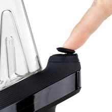 A close-up shows a hand pressing the power button on a black and silver New Peak Vaporizer, with part of its glass 3D Chamber visible.