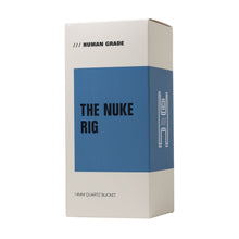 Minimalist white and blue box labeled "Human Grade The Nuke Glass Rig." Packaging hints at a borosilicate glass dab rig inside with a 14MM quartz bucket and possibly a distinct mushroom cloud perc design.