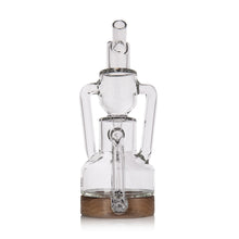 The MJ Arsenal Alpine Series - Apex Mini Rig is a clear glass water pipe with a modern design, two side arms, and a cylindrical mouthpiece, displayed on a wooden base against a white background.