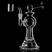 The MJ Arsenal Apollo Mini Dab Rig is a clear borosilicate glass piece with a bulbous body, angled mouthpiece, and attached quartz banger, engineered for optimal flavor and shown against a solid black background.