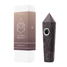 A pointed, dark Gemstone Pipe with a replaceable mesh bowl rests beside a white and brown “Astral Project” box labeled “Astrophyllite,” featuring a geometric logo and minimalist design.