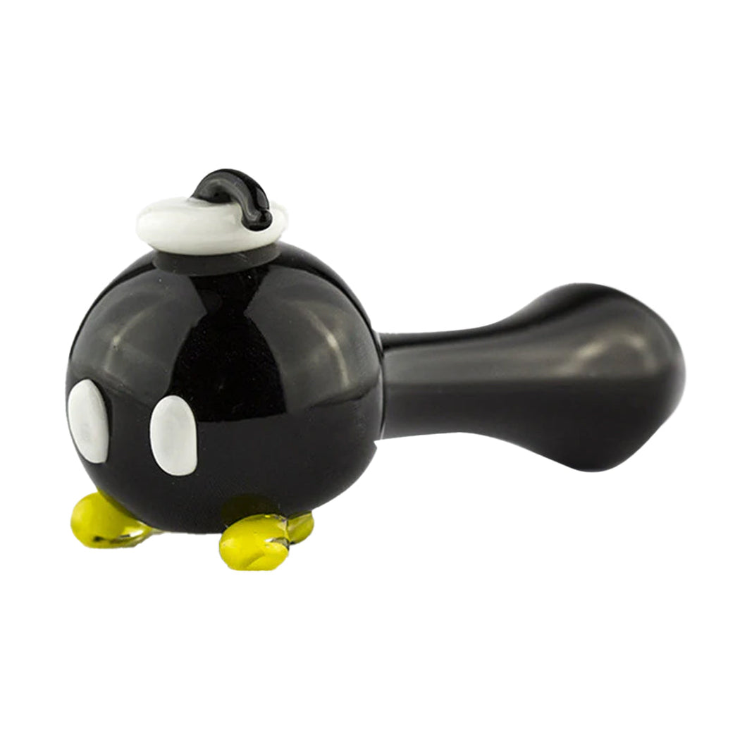The Empire Glass Works Bomber Dry Pipe is a handcrafted spoon pipe shaped like a black cartoon bomb with white eyes, yellow feet, and a white wick tip, inspired by the iconic Bob-omb character from video games.