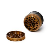 The Human Grade Grinder 7F (2.5") is a two-piece aluminum herb grinder with sharp teeth, featuring a gold and black finish. One half lies flat while the other stands upright, both displayed on a white background.