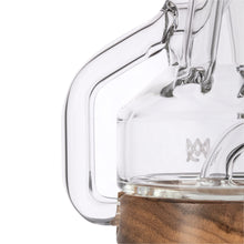 Close-up of a clear glass coffee carafe with a thick handle and wooden base, reflecting the detailed craftsmanship and smooth lines of the MJ Arsenal Alpine Series - Apex Mini Rig.