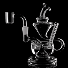 The MJ Arsenal Claude Mini Dab Rig, a clear glass recycler with intricate curves and chambers, is displayed against a black background. It features multiple tubes, a cup-shaped attachment, and a stable round base for enhanced function and style.