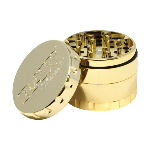 The RAW Ethereal Grinder features a shiny gold-plated, reflective finish. Its partially open lid, embossed with 