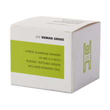 White box with green accents labeled “HUMAN GRADE,” containing the Human Grade Grinder 2A (2.5" 4-Piece)—an aluminum grinder with pollen screen, rugged notched design, scraper tool, and a green abstract symbol on the side.