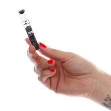A hand with red nails and a tattoo holds the GRAV 12mm Glass Tasters Display vial with a black cap against a white background—ideal for showcasing sleek glass pipes.