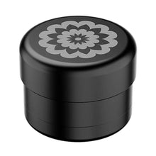 The Flower Mill 2" Next Gen Premium Grinder is a black cylindrical grinder with a gray geometric flower pattern on the lid, offering a sleek look. It fits 2" mill plates and ensures medium grind consistency. Set against a white background.