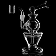 The MJ Arsenal Gemini Mini Dab Rig, made from borosilicate glass, stands on a black background. Water bubbles through its intricate chambers as vapor flows inside this compact and portable dab rig.