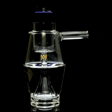 The MJ Arsenal Proxy Bubbler, made of clear borosilicate glass, features a cylindrical side handle, a gold logo on the body, and a water-holding base. It is shown against a black background and resembles the style of a traditional bubbler.