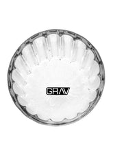 A clear, round borosilicate glass ashtray with a scalloped edge and “GRAV” in bold black letters on the bottom—an ideal accessory to use with your GRAV® Monarch Gravity Bong.
