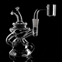 The MJ Arsenal Hydra Mini Dab Rig, made of clear glass with a twisting design and wide base, is displayed against a black background. Its quartz banger attachment is visible on the right side.