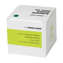 The Human Grade Grinder 6M (2.5") is an ergonomic 4-piece aluminum grinder with a mirrored finish and scraper tool, packaged in a white box with minimalist green and black HUMAN GRADE graphics.