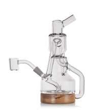 The MJ Arsenal Alpine Series - Apex Mini Rig features clear glass, a wooden base, angled mouthpiece, and side handle for smoking or vaporizing. Inspired by MJ Arsenal designs and displayed against a white background.