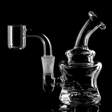 The MJ Arsenal Jammer Mini Dab Rig, crafted from clear borosilicate glass with a bent neck and quartz banger, is displayed on a reflective black surface with dramatic lighting—an eye-catching, portable dab rig for your collection.