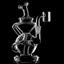 The MJ Arsenal Mini Jig Mini Dab Rig, made from clear glass with intricate twists and loops, rotates against a black background—highlighting its stylish design and practical function for concentrate enthusiasts.