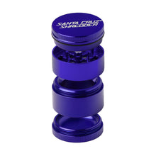 A blue Santa Cruz Shredder Medium 4-Piece Grinder is shown with its compartments separated and stacked vertically, displaying the internal grinding teeth and chambers.