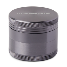 The Human Grade Grinder 1A (2" 4-Piece) is a metallic grinder with a textured grip, pollen screen, and "HUMAN GRADE" engraved on the top lid.