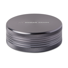 The Human Grade Grinder 1C (2.5" 2-Piece) is a round, silver aluminum grinder with textured sides and "HUMAN GRADE" engraved on the smooth top. Durable and stylish, it's perfect for any grinding need.