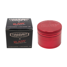 A red Hammercraft x RAW 2.2" Grinder sits beside its black box packaging labeled Hammer Craft x RAW Natural Rolling Papers, featuring a 4-piece aluminum design.