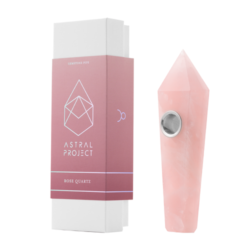 The Gemstone Pipe, made from rose quartz and featuring a replaceable mesh bowl, stands next to its pink and white box labeled “Astral Project Gemstone Pipe – Rose Quartz,” delivering a premium crystal smoking experience.