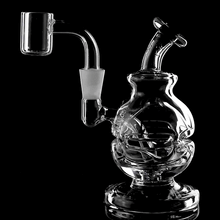 The MJ Arsenal Royale Mini Dab Rig is a clear borosilicate glass piece with intricate internal tubing, a fab egg percolator, and a quartz banger, shown against a solid black background.
