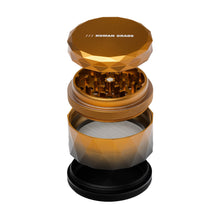A gold, 4-piece Human Grade Grinder 7F (2.5") aluminum herb grinder with HUMAN GRADE on the lid, shown separated to reveal its sharp teeth, mesh screen, and collection chamber against a white background.