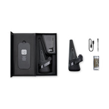 A black New Peak Vaporizer kit is open, showing the device with 3D Chamber, accessories, and instruction card on the left; on the right are the Puffco New Peak Vaporizer, charging cable, loading tool, and extra parts arranged neatly.