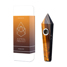 The Gemstone Pipe, featuring a pointed tip and brown tiger eye pattern, is shown next to its Astral Project box. This crystal pipe has a small replaceable mesh bowl embedded for convenience.