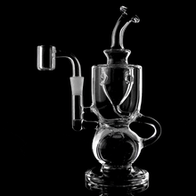The MJ Arsenal Titan Mini Dab Rig, crafted from clear borosilicate glass with intricate curves and chambers, is displayed against a black background, highlighting its detailed design and expert craftsmanship.