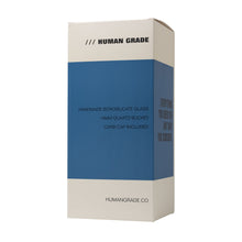 A white and blue rectangular box labeled HUMAN GRADE holds the Human Grade 10" Mini Gumball Rig Glass Water Pipe, plus a 14mm quartz bucket and carb cap. The website humangrade.co is printed at the bottom.